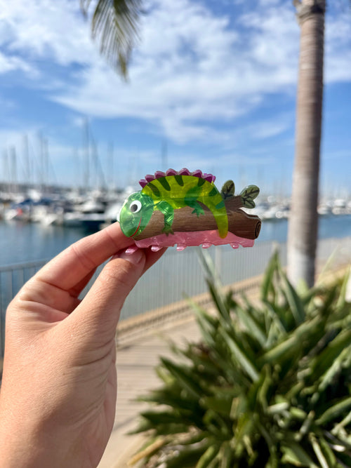 Chameleon hair claw clip in translucent green with pink spines, perched on a brown log