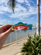 Rainbow trout hair claw clip held up in front of a marina