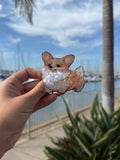 Peeking corgi face hair claw clip held up against marina background